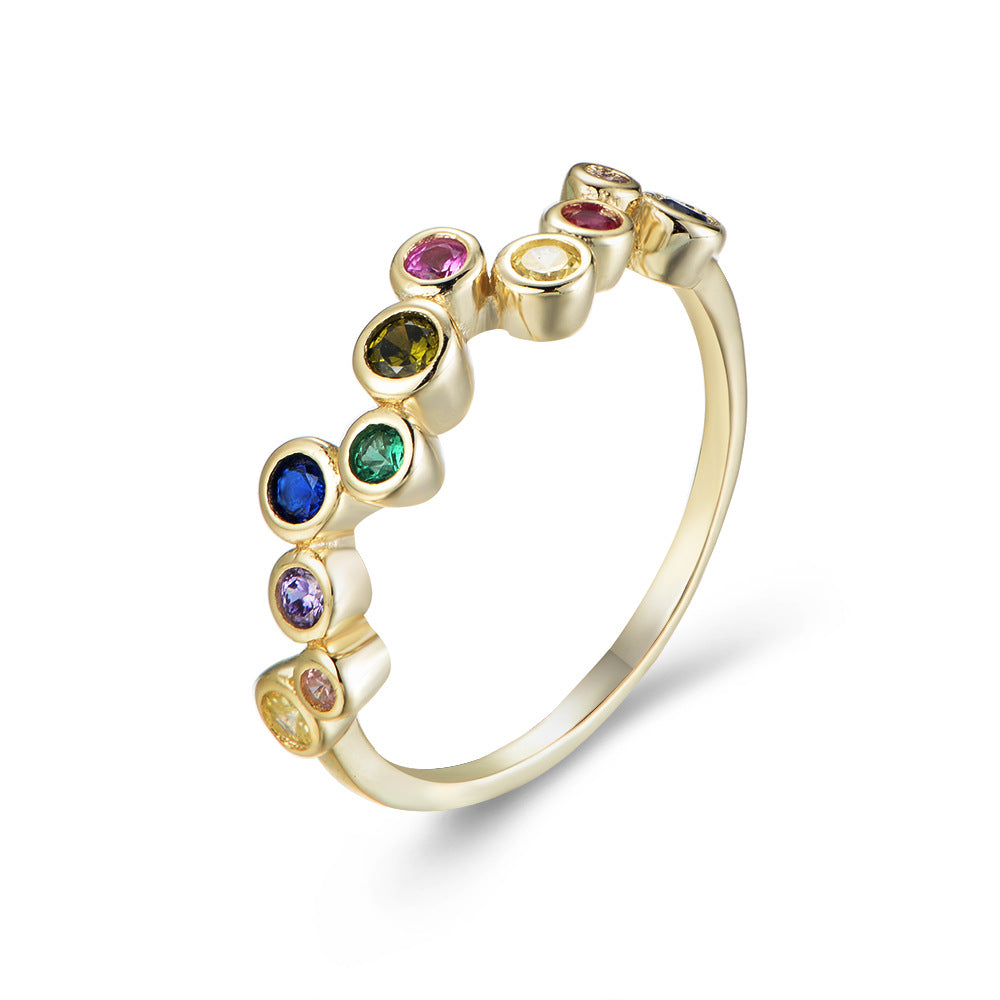 A gold dainty rainbow bubble ring with multicolored gemstones in bezel settings displayed against white backdrop