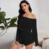 Front view of woman modeling black off-shoulder romper with long sleeves on white couch with plant decor
