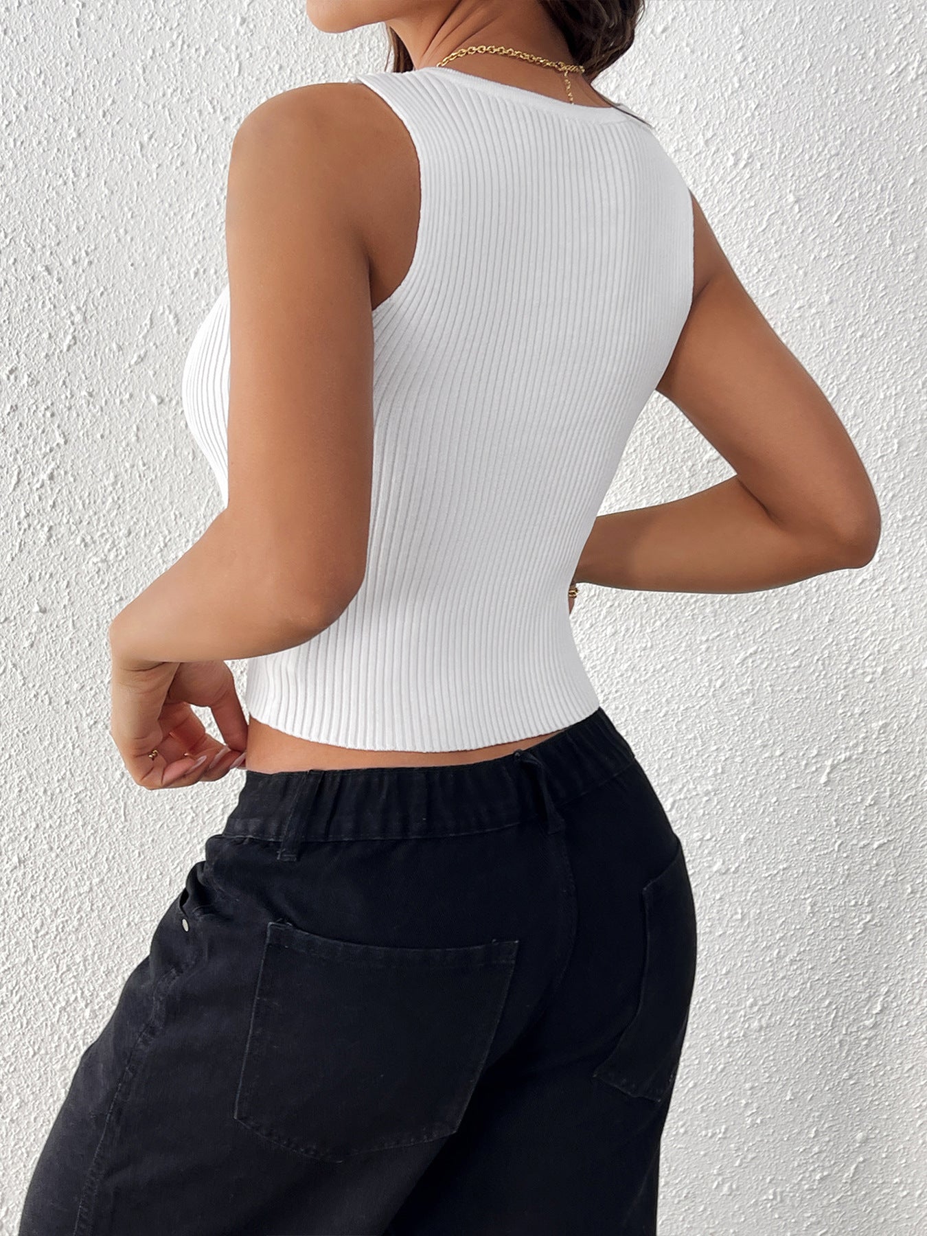 Back view of a woman wearing a white ribbed sleeveless crop top and high-waisted black pants, highlighting the fitted silhouette.