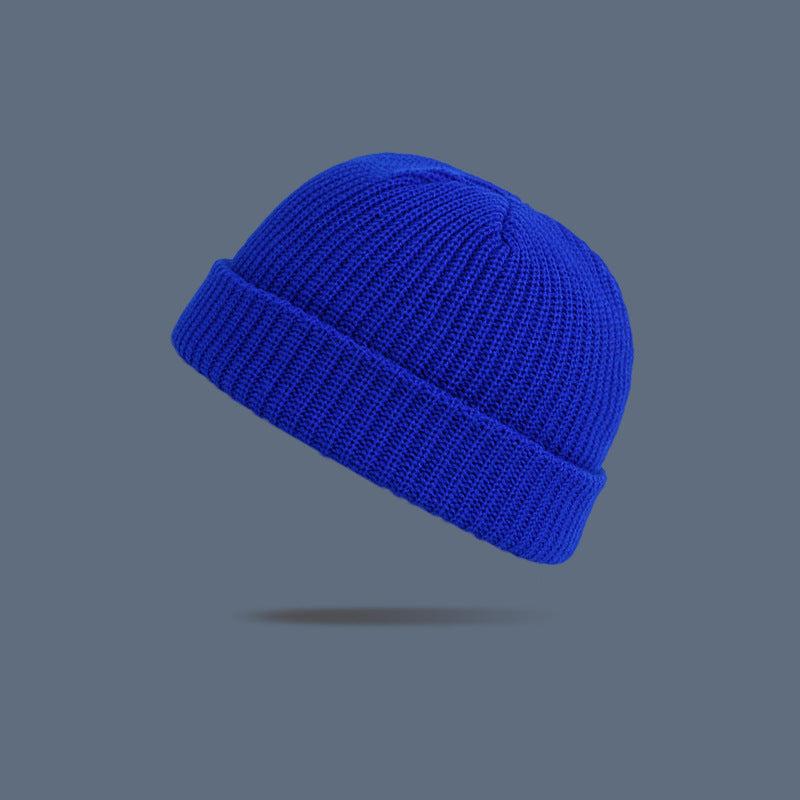 A royal blue ribbed knit beanie with folded cuff floating against slate gray background, displaying classic winter hat design