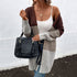Brown and gray color-block oversized cardigan styled with white tank top, blue jeans, and black fringe handbag