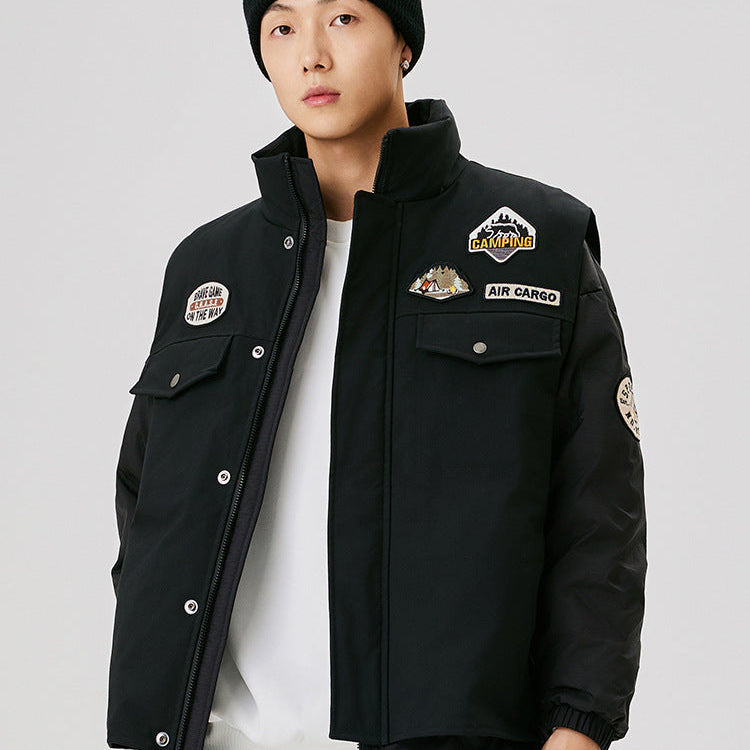Front view of black outdoor jacket with camping and brave game patches, worn with white t-shirt and black beanie