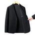 Black textured blazer displayed on wooden hanger with partially opened front showing inner lining and hand pointing to interior pocket