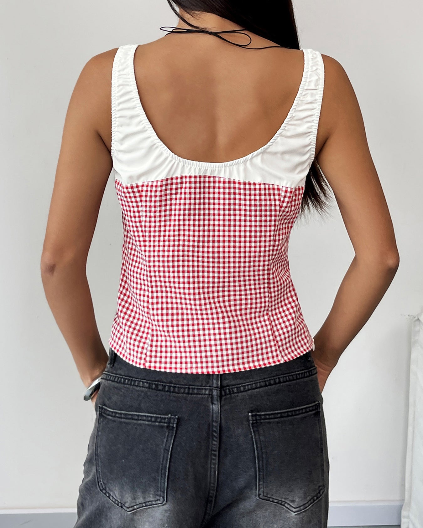 Back view of a woman in a red and white gingham tank top with a white ruched trim, highlighting the fitted cut and sleeveless design.