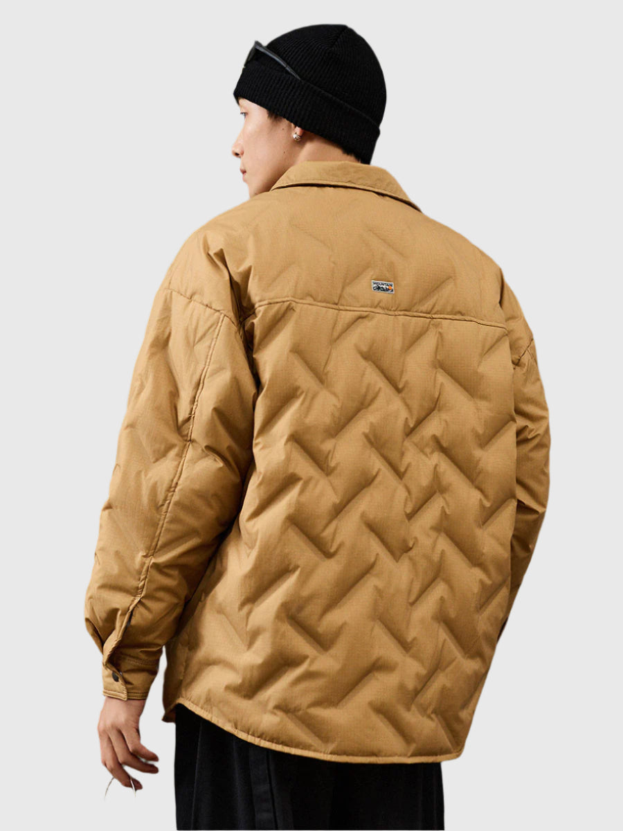 Back view of a man wearing black beanie and tan quilted jacket with diagonal pattern, showing brand logo patch
