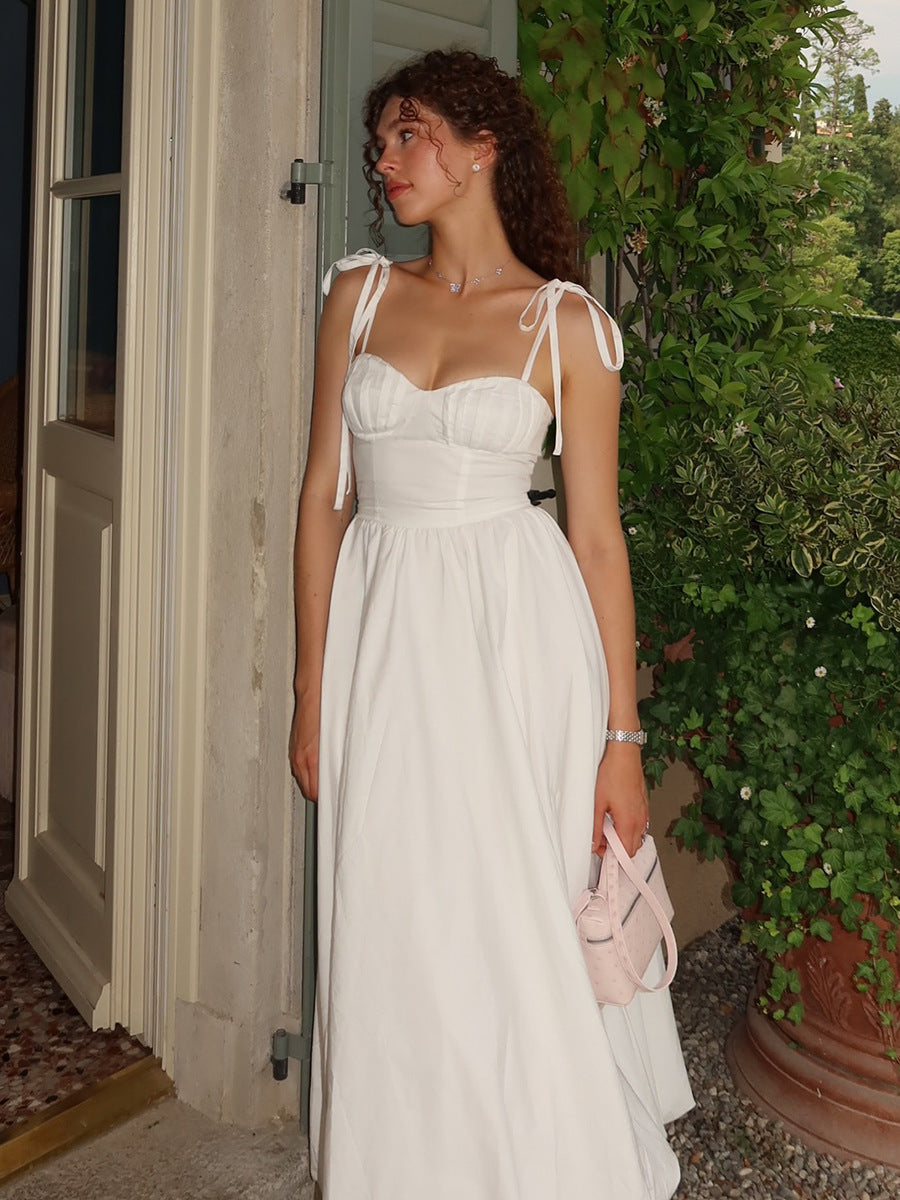 Woman in a white dress standing outside a building with greenery in the background