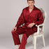 Man sitting in ornate white chair wearing burgundy striped silk pajamas with notched collar and relaxed long sleeves