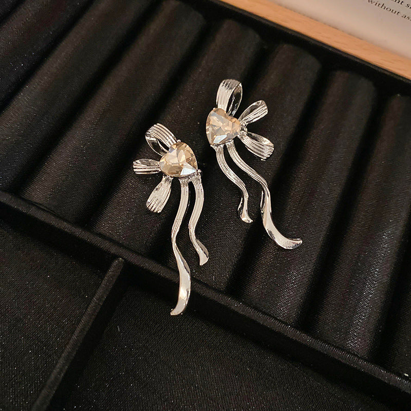 Simple silver bow earrings with heart-shaped crystal centers displayed on black velvet jewelry tray