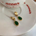 Small gold hoop earrings with deep green stone pendants on white porcelain dish with red script text showing dainty elegant design