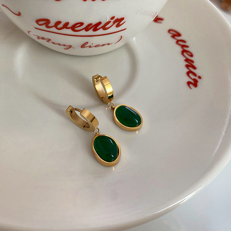 Small gold hoop earrings with deep green stone pendants on white porcelain dish with red script text showing dainty elegant design