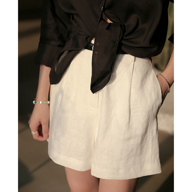 Detail shot of white linen shorts with side pocket detail, shown with black blouse in moody lighting