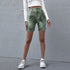 Model stands with legs slightly apart, wearing green tie-dye biker shorts and a white long-sleeve cropped top
