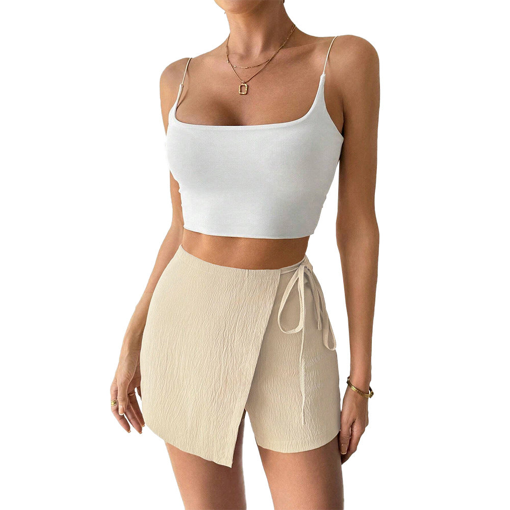 Minimalist summer two-piece set featuring white spaghetti strap crop top and cream wrap-style skort with gold accessories