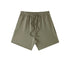 Olive green cotton shorts with elastic waistband and drawstring, featuring relaxed fit and clean minimal design against white background