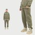 Man wearing olive green tracksuit set with necklace. Close-up shows slide sandals with white socks against white background