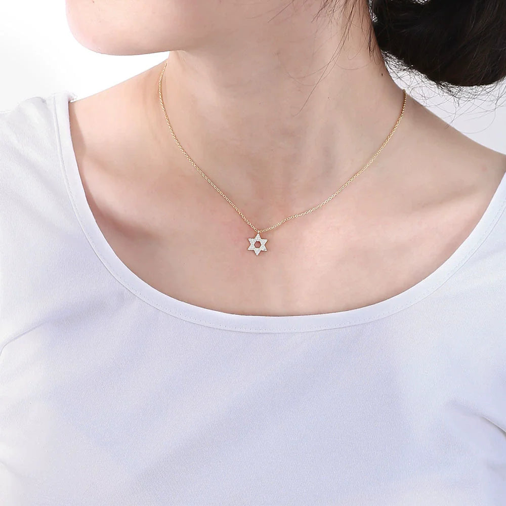A woman wearing a white t-shirt with a gold Star of David necklace. The delicate pendant rests at her collarbone on a thin gold chain