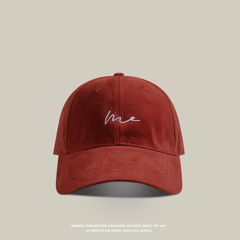 Red baseball cap with 'Me' embroidered in white cursive, soft washed fabric, and a classic curved brim