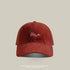 Red baseball cap with 'Me' embroidered in white cursive, soft washed fabric, and a classic curved brim