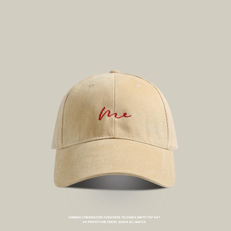 Khaki baseball cap with 'Me' embroidered in white cursive, washed fabric, and adjustable back strap