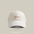 Beige baseball cap with 'Me' embroidered in red cursive, featuring a curved brim and vintage washed look