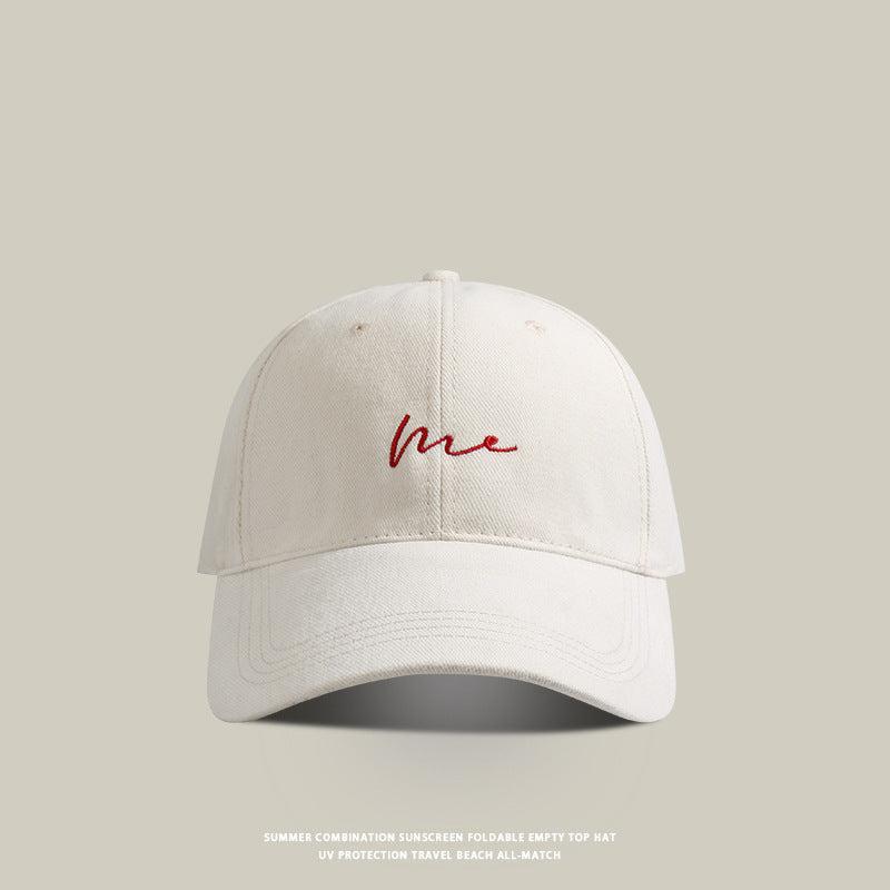 Beige baseball cap with 'Me' embroidered in red cursive, featuring a curved brim and vintage washed look