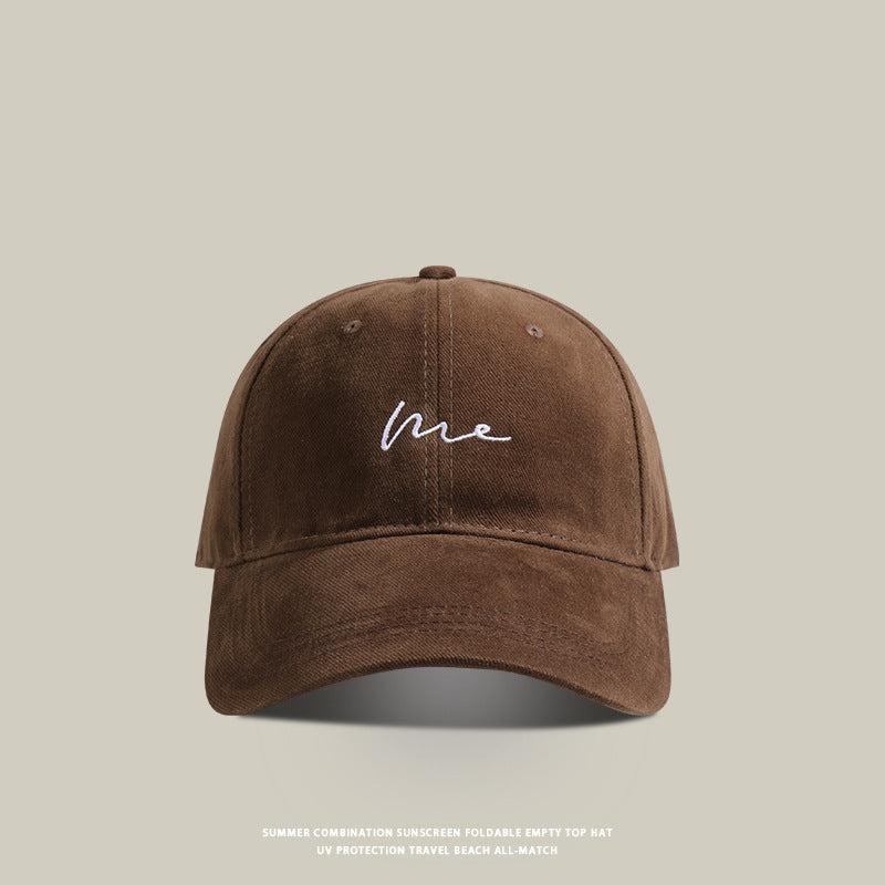 Coffee brown baseball cap with 'Me' embroidered in white cursive, featuring a curved brim, washed cotton fabric, and an adjustable strap for a relaxed fit