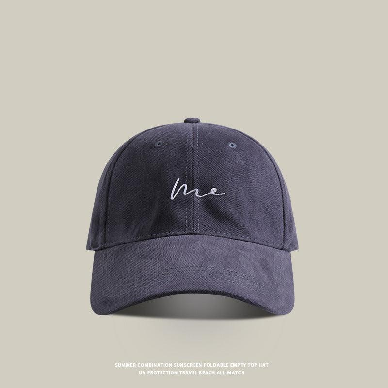 Navy blue baseball cap with 'Me' embroidered in white cursive, adjustable strap, and a classic streetwear fit