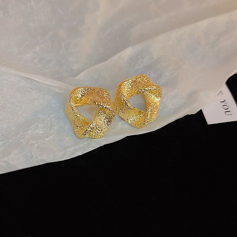 Textured Gold Twisted Hoop Earrings – Unique gold earrings with a sculptural twisted design and a rough textured finish, set against crinkled paper