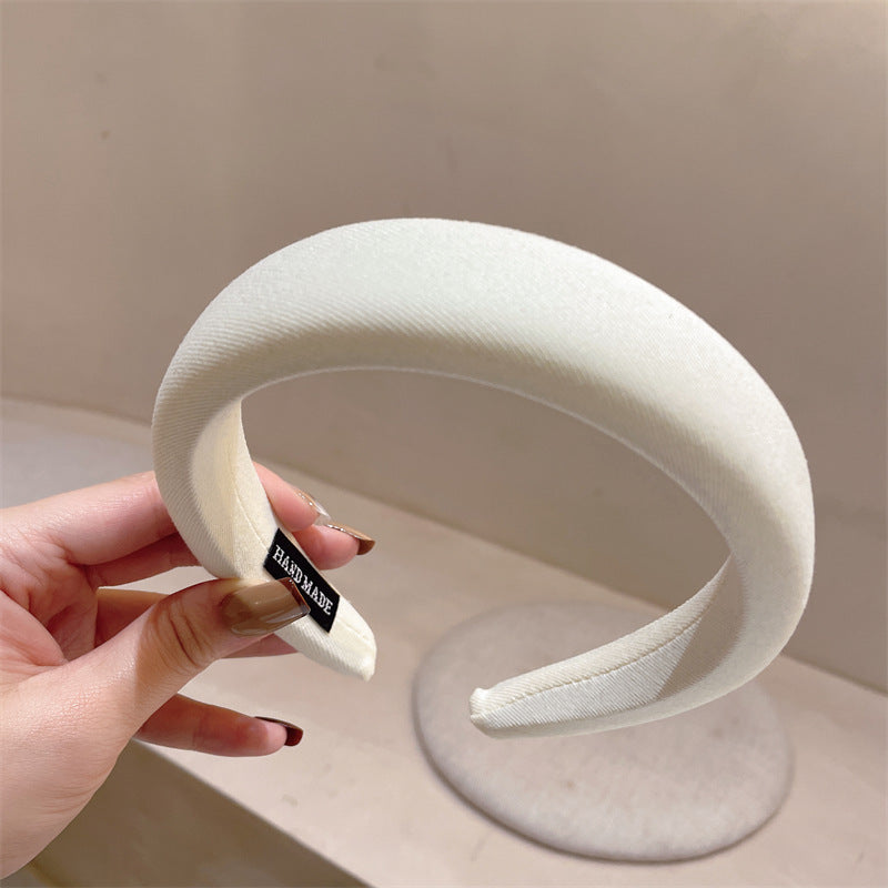 Close-up of a white padded fabric headband with a "handmade" tag, held in a hand
