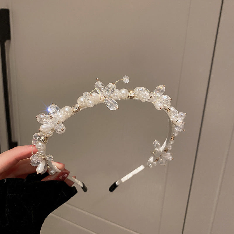 Pearl and crystal floral headband with butterfly details, held against a neutral background