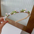 Gold floral pearl headband with green leaf accents, displayed against a glass-paneled background