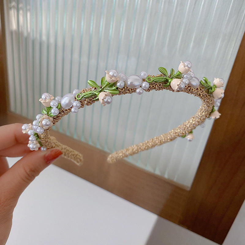 Gold floral pearl headband with green leaf accents, displayed against a glass-paneled background