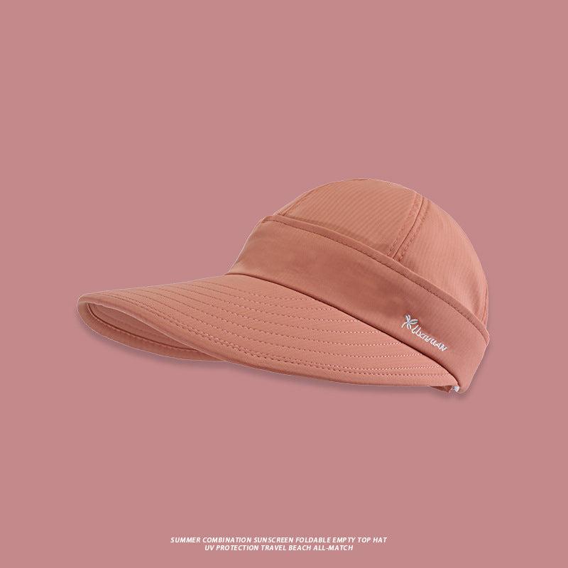 A camel-colored foldable sun visor with wide brim and embroidered logo detail displayed against soft pink background