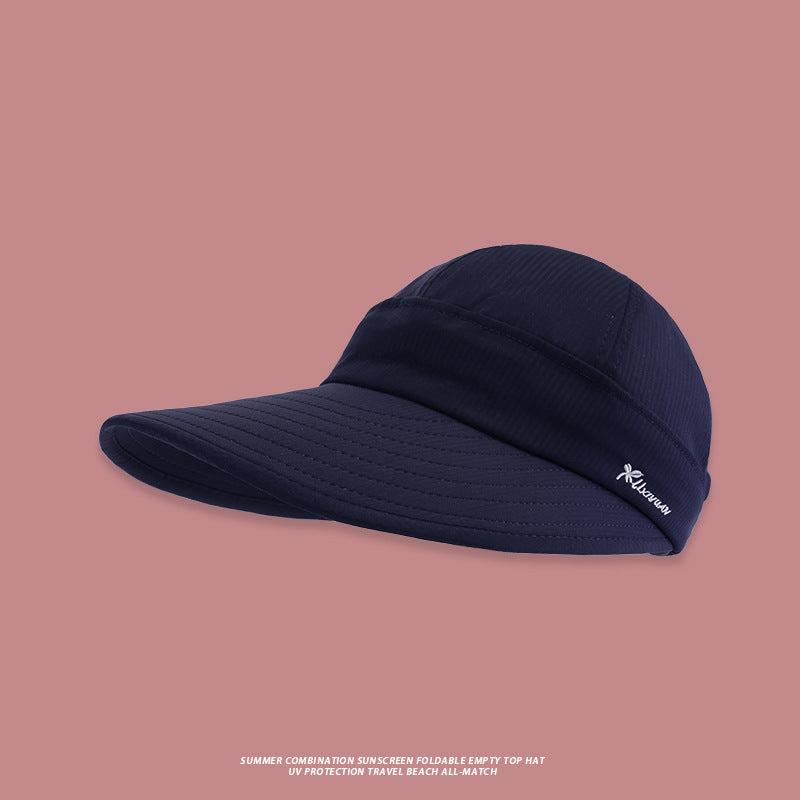 A navy blue structured sun visor with wide brim and white embroidered logo detail presented against pink backdrop