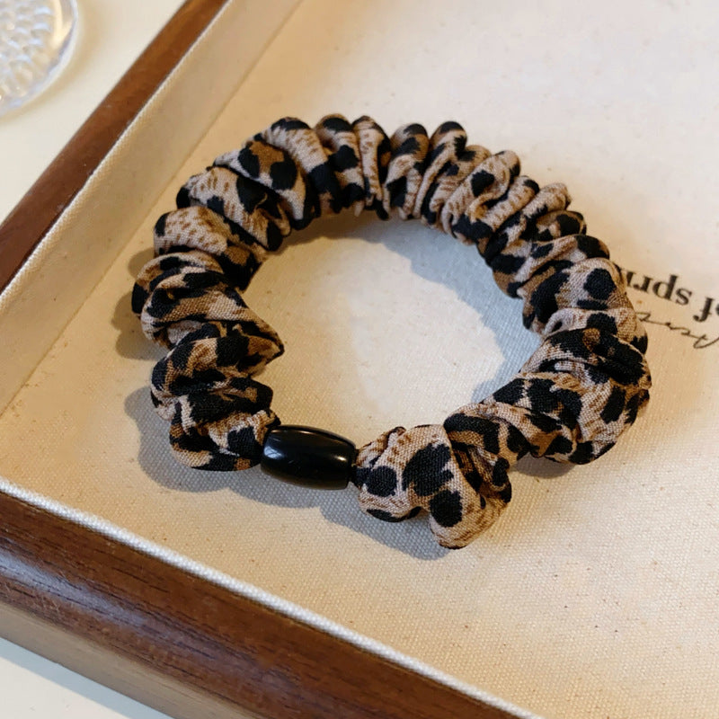Close-up of leopard print scrunchie with black bead detail displayed on fabric-lined wooden tray surface