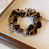 Leopard print scrunchie with brown accent bead arranged on canvas tray surface, showing detailed fabric pattern