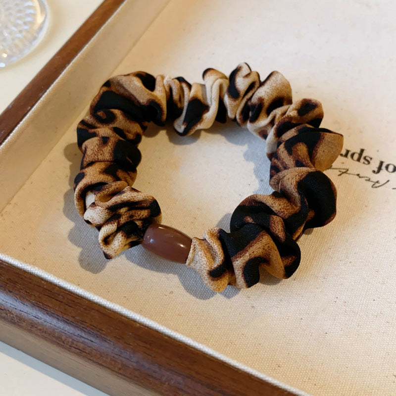 Leopard print scrunchie with brown accent bead arranged on canvas tray surface, showing detailed fabric pattern