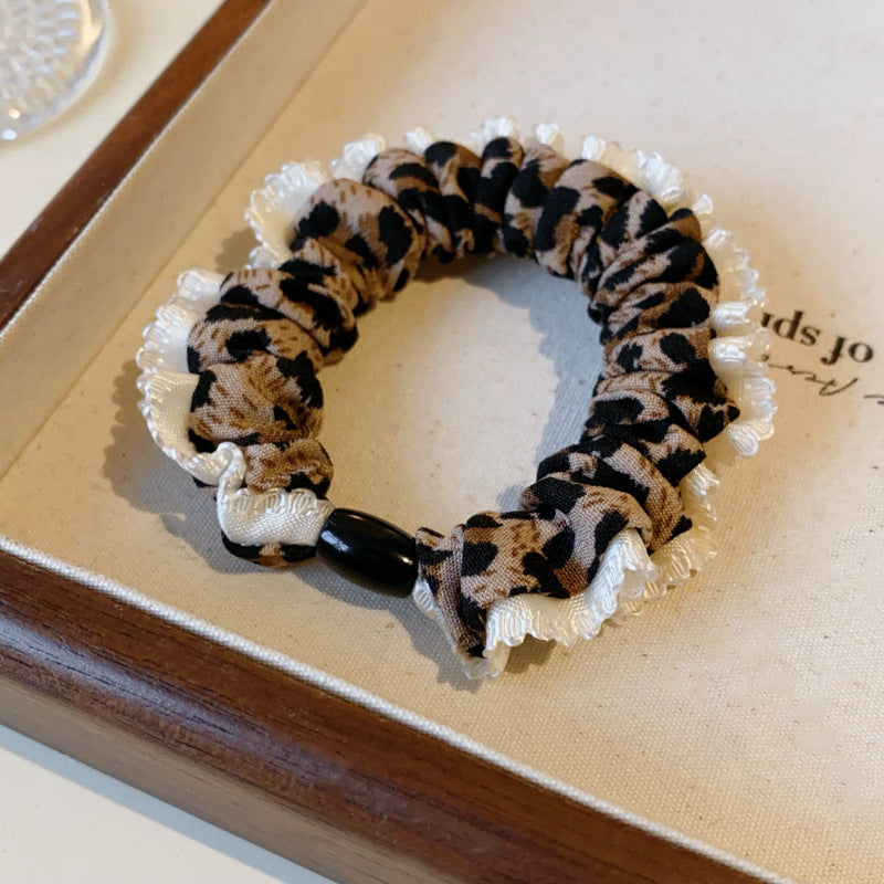 Close-up of leopard print scrunchie with white lace trim and black accent bead displayed on decorative tray