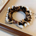 Detailed view of leopard print scrunchie with white ruffle trim and brown bead accent on display tray against neutral background