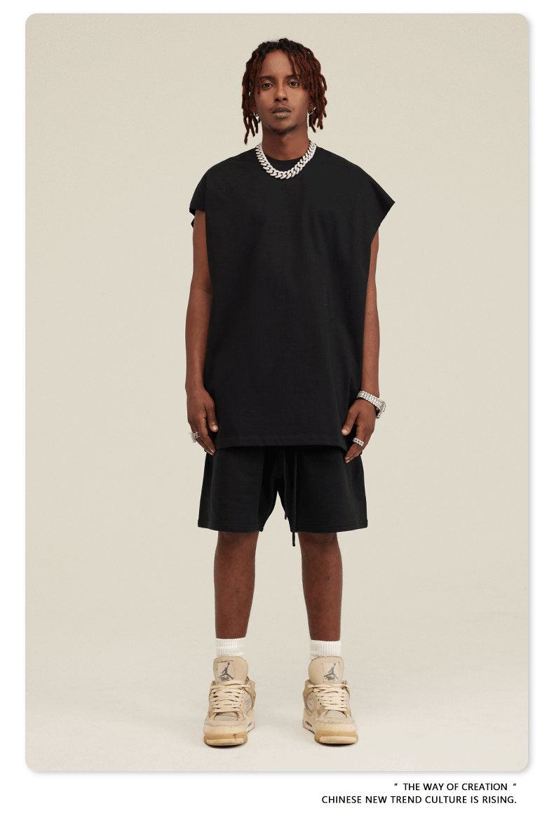 Male model wearing black oversized tee and matching shorts with beige Jordan sneakers and silver jewelry