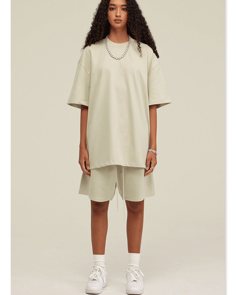 Woman with curly hair modeling cream oversized T-shirt and shorts set with white sneakers and silver chain necklace