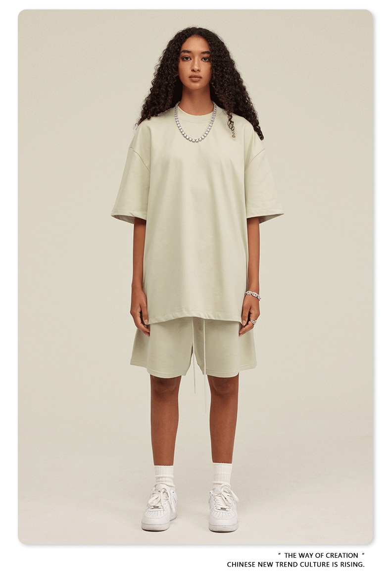 Woman with curly hair modeling cream oversized T-shirt and shorts set with white sneakers and silver chain necklace