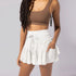 Model wearing white tiered tennis skirt with drawstring waist and brown sports bra, showing ruffle detail against gray backdrop