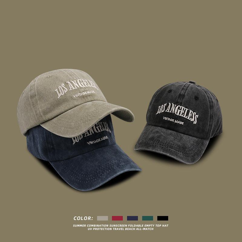Three Los Angeles baseball caps in beige, navy blue and black washed cotton with white embroidered logo on neutral backdrop