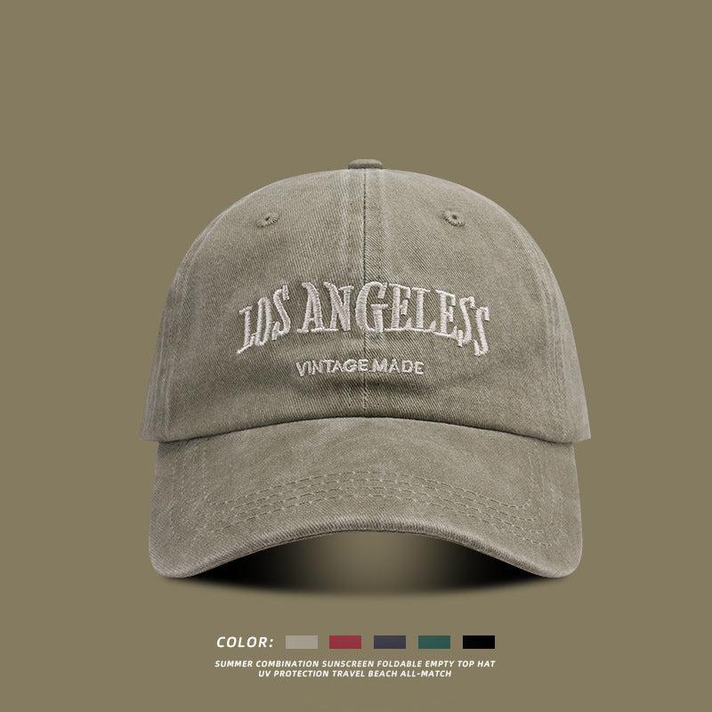 Beige washed cotton baseball cap with white 'LOS ANGELES VINTAGE MADE' embroidery on front against olive background