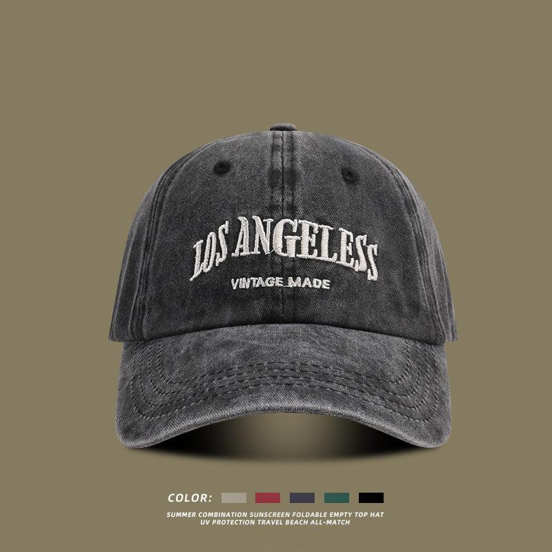 Charcoal gray washed cotton baseball cap with white embroidered Los Angeles text against neutral background