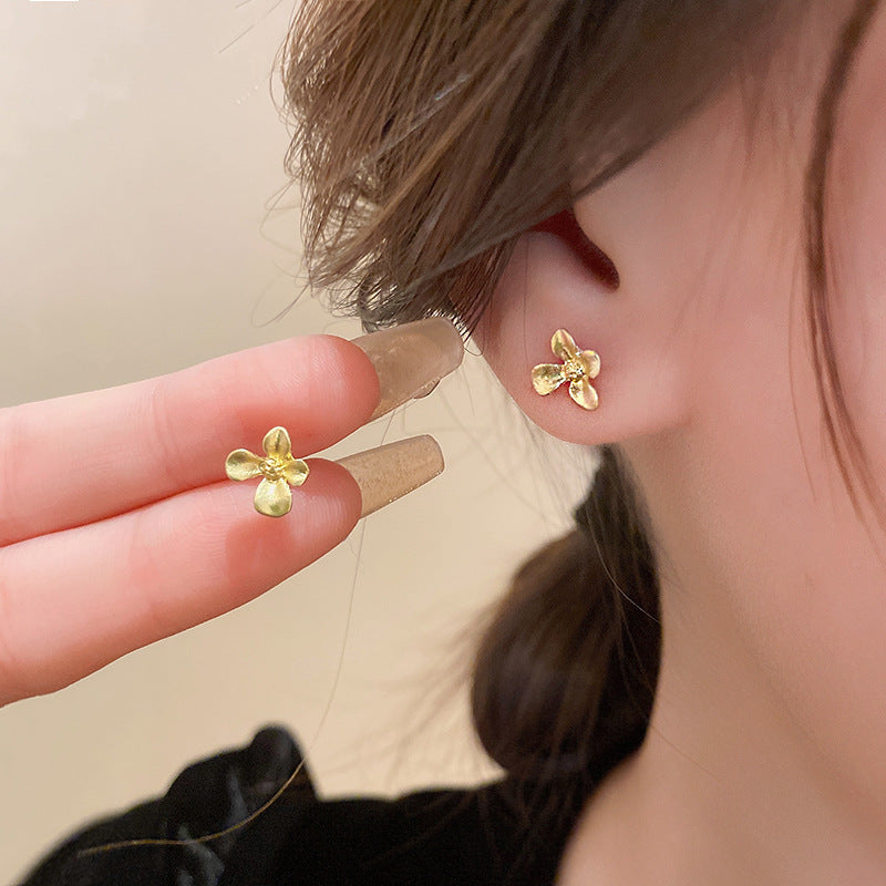 Gold flower stud earrings close-up showing delicate petal detail