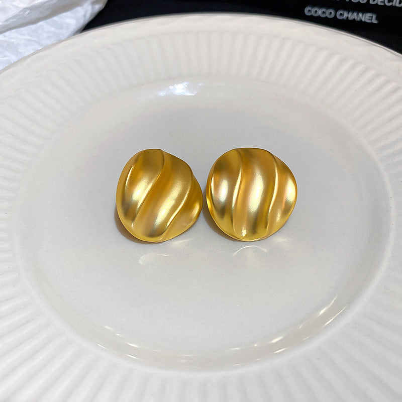 Gold pleated circle earrings with ripple texture on white plate