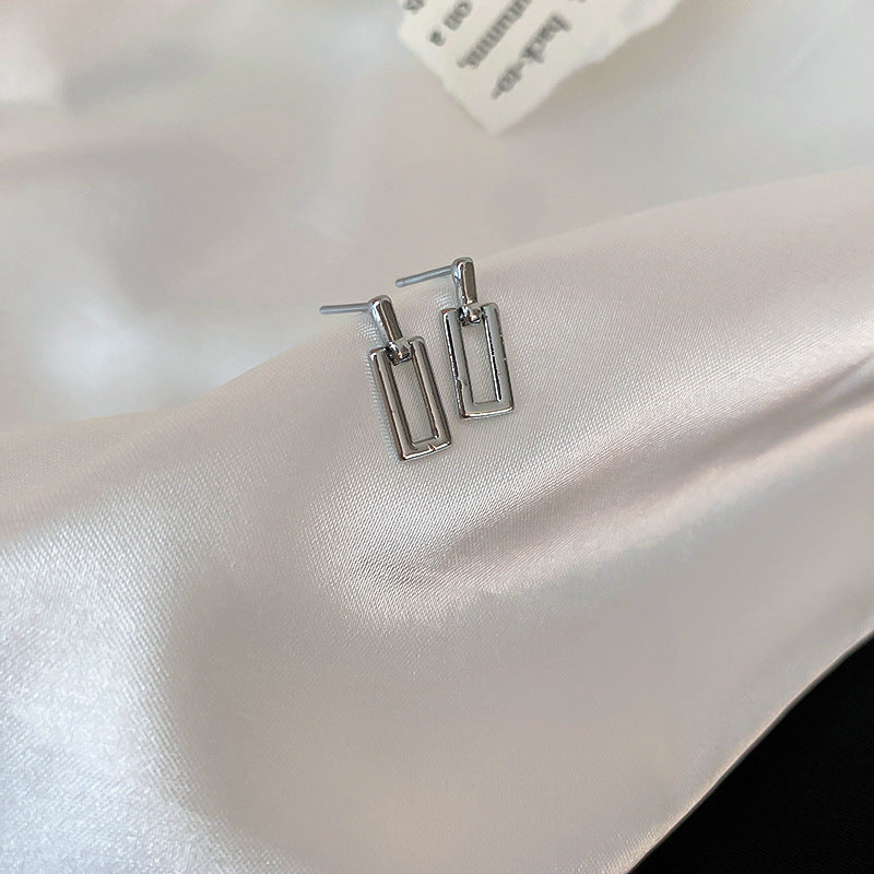 Silver minimalist square earrings on silk background