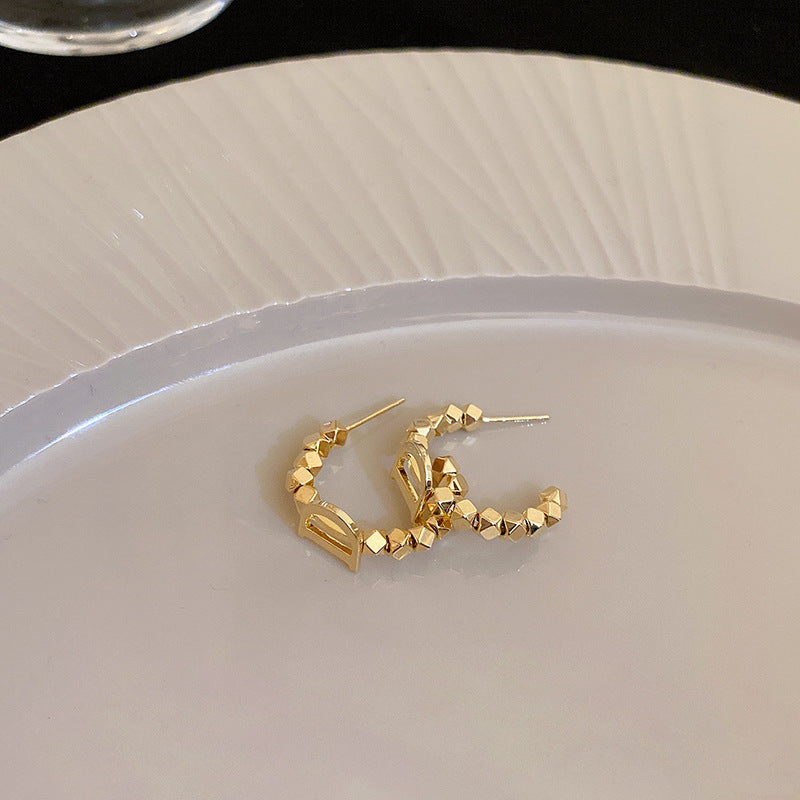 Gold geometric hoop earrings with faceted cube beads on white plate, modern minimalist C-shaped design